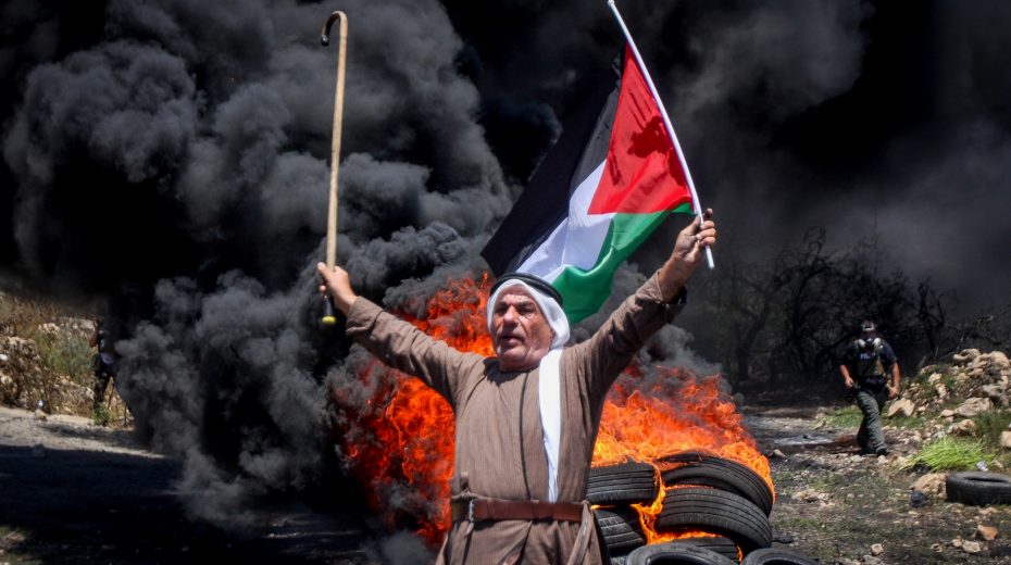 Palestinian protester stands in front of a pile of burning tires