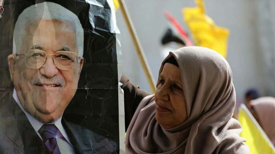 A Palestinian woman looks on unimpressed at a photo of Palestinian Authority President Mahmoud Abbas.