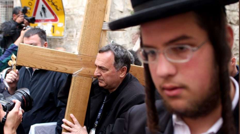 Ein orthodoxer jüdischer Mann zeigt sich unbeeindruckt, höchstens etwas genervt, als Christen mit einem großen Holzkreuz in der Jerusalemer Altstadt vorbeigehen.