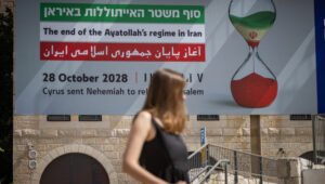 People walk next to a large sign written "the end of the Ayatollah's regime in Iran" on a building, May 20, 2024. Photo by Chaim Goldberg/Flash90