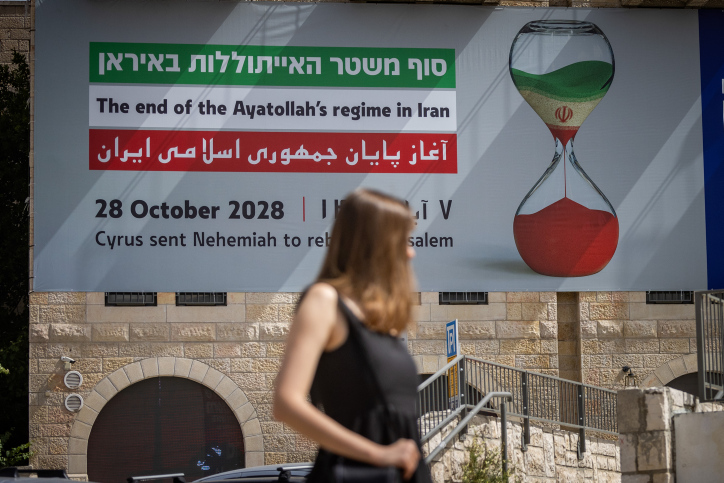 People walk next to a large sign written "the end of the Ayatollah's regime in Iran" on a building, May 20, 2024. Photo by Chaim Goldberg/Flash90
