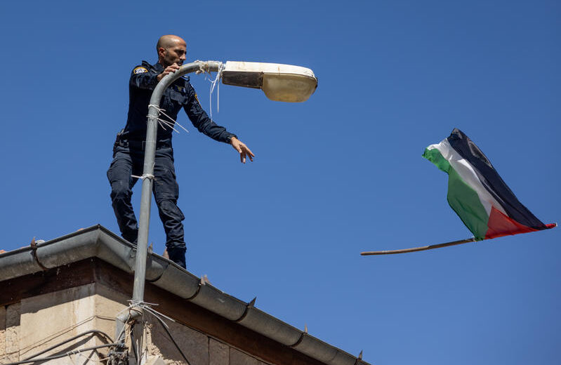 An Israeli police officer tosses a Palestinian flag off the top of a building in Jerusalem. Photo by Chaim Goldberg/Flash90