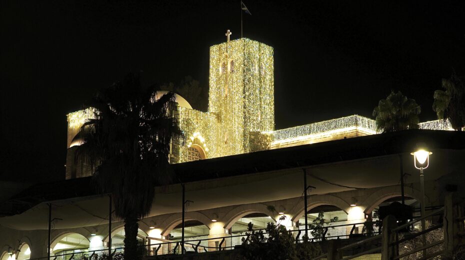 The church tower of St. Andrews, with the Scottish flag waving in the wind, rises into the night sky, behind palm trees and the terrace of the Menachem Begin Memorial. Photo: Moshe Gruenbauer