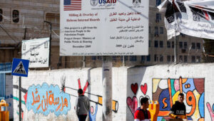 Palestinians walk under a sign of the U.S. Agency for International Development (USAID) project in Hebron in the West Bank on February 5, 2019. Photo by Wisam Hashlamoun/Flash90