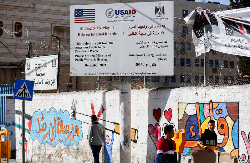 Palestinians walk under a sign of the U.S. Agency for International Development (USAID) project in Hebron in the West Bank on February 5, 2019. Photo by Wisam Hashlamoun/Flash90