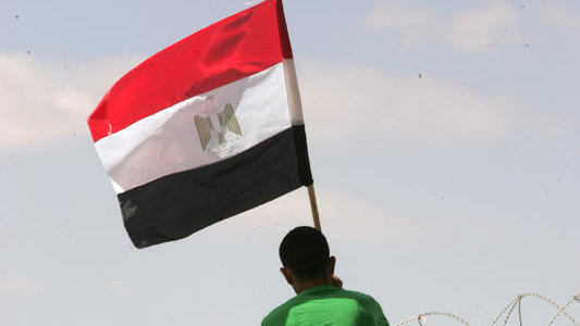 A Palestinian man raises an Egyptian flag at the Sinai-Gaza border. Photo by Abed Rahim Khatib/Flash90