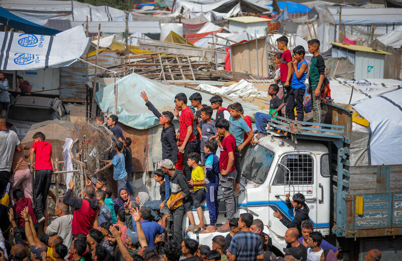 Displaced Palestinians reach out for bread being distributed through a bakery window in Nusseirat Refugee Camp, in the central Gaza Strip, May 22, 2025. Photo by Ali Hassan/Flash90