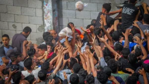 Gazans reach out for bags of pitas being distributed through a bakery window in the Nusseirat camp, in the central Strip, May 22, 2025. Photo by Ali Hassan/Flash90.