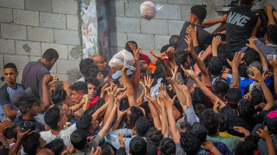 Gazans reach out for bags of pitas being distributed through a bakery window in the Nusseirat camp, in the central Strip, May 22, 2025. Photo by Ali Hassan/Flash90.