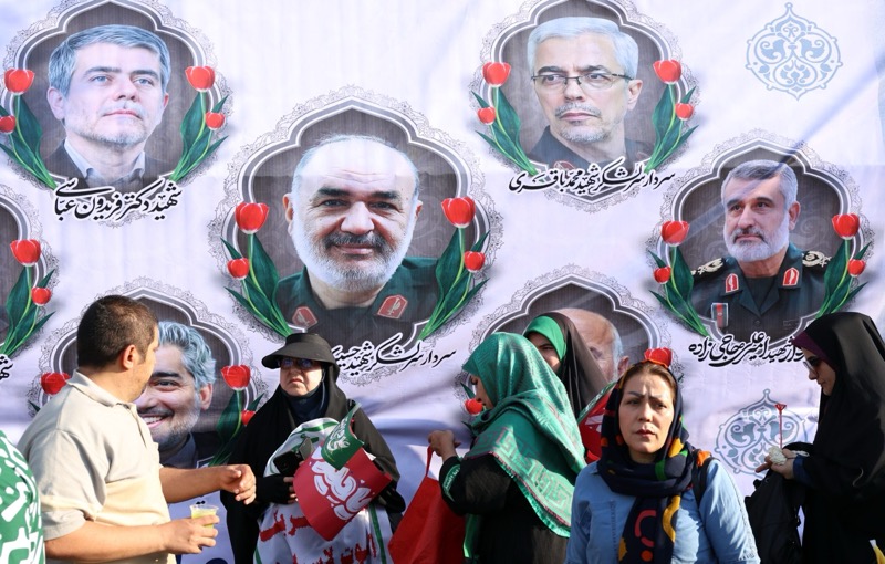 Iranians stand in front of a billboard depicting five killed high-ranking Iranian regime officials: Chief of General Staff Mohammad Bagheri, IRGC Commander Hossein Salami, Air Force Chief Amir Ali Hajizadeh, and nuclear scientists Fereidun Abbasi and Mohammad Mehdi Tehranchi. Photo: EPA-EFE/Abedin Taherkenareh.