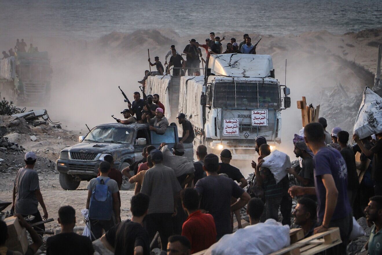 Armed Palestinians sit on trucks carrying humanitarian aid near the Zikim border crossing between Israel and Beit Lahia in the northern Gaza Strip, Aug. 18, 2025. Photo by Khalil Kahlout/Flash90.
