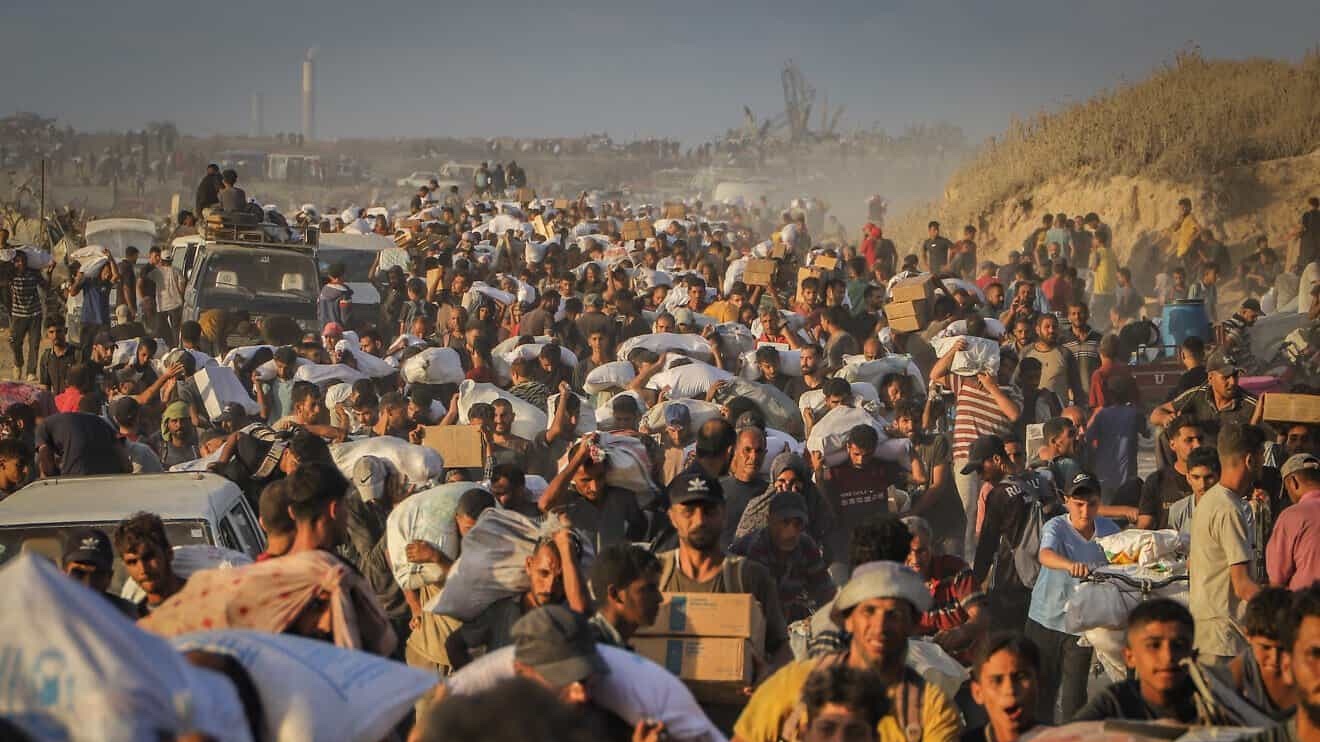 Palestinians carry food parcels and supplies from aid trucks near the Zikim border crossing between Israel and Beit Lahia, in the northern Gaza Strip, Aug. 18, 2025. Photo by Khalil Kahlout/ Flash90.