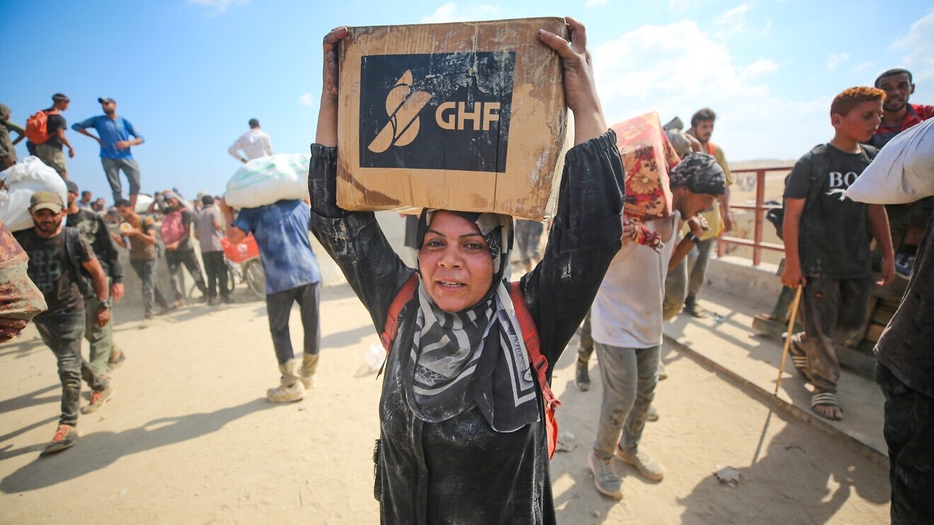 Palestinians carry food and supplies from a Gaza Humanitarian Foundation aid distribution point at the Netzarim Corridor in the central Strip, Aug. 1, 2025. Photo by Ali Hassan/Flash90.