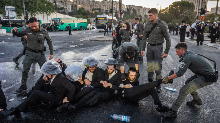 Ultra-Orthodox Jewish men block a street and clash with police in Jerusalem during a protest against the arrest of three yeshiva students who refused to be drafted (July 2025). Photo: Chaim Goldberg/Flash90