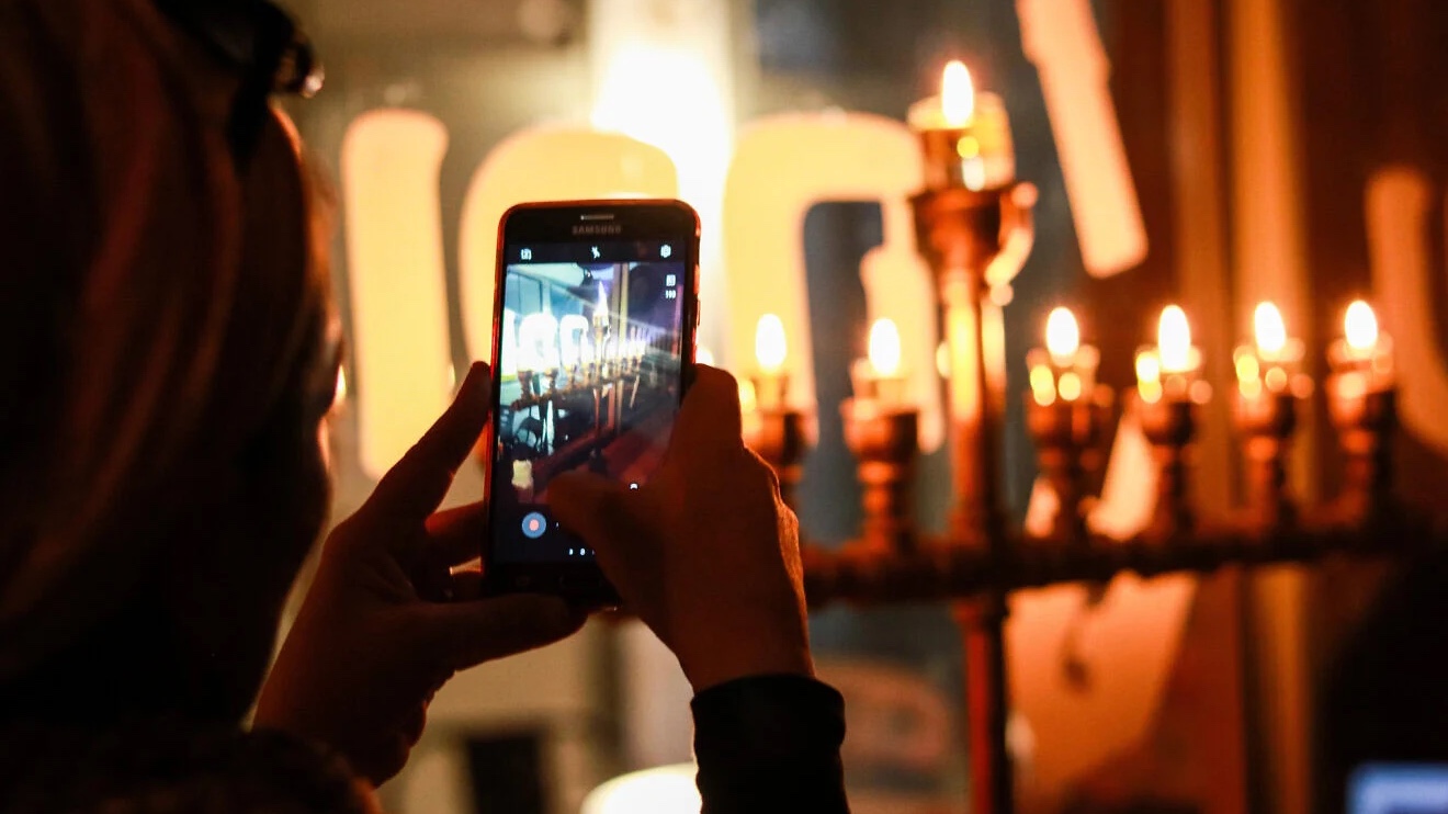 A women takes a photograph of a menorah (chanukiyah) at Mahane Yehuda outdoor market in Jerusalem, Dec. 9, 2018. Photo by Liba Farkash/Flash90.