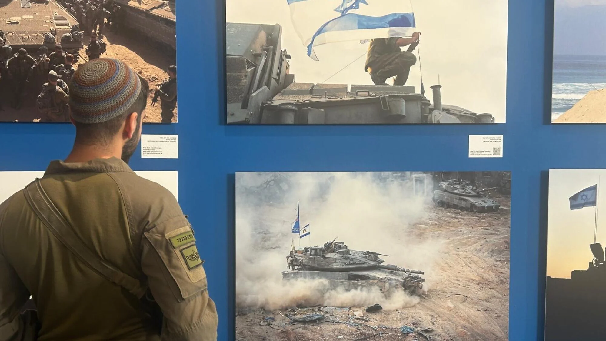 Staff Sgt. Y. looks at a picture he took at the start of “Operation Gideon’s Chariot” in May 2025, when he accompanied Givati infantrymen to Jabalia, near Gaza City, at the “Moments that Remain” exhibition at the Rabin Center in Tel Aviv, December 2025. Photo by Amelie Botbol.