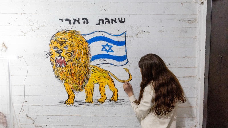 An Orthodox Jewish woman paints a lion with the words "Operation Lion’s Roar," in a public shelter in Petach Tikva during an air raid siren. Photo by Chaim Goldberg/FLASH90