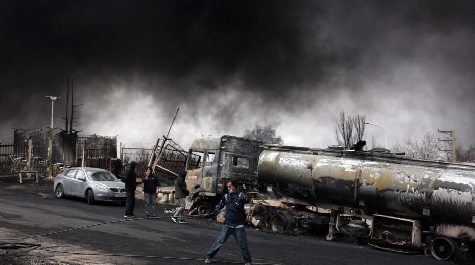 Dark smoke envelops destroyed vehicles near a still-burning fire that erupted after a nighttime airstrike on the Shahran oil refinery northwest of Tehran on March 8, 2026. Photo: EPA/ABEDIN TAHERKENAREH