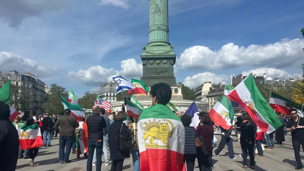 A man drapped in a shah-era flag at a rally in support of the Iranian people at Place de la Bastille in Paris, April 19, 2026. Photo by Amelie Botbol.