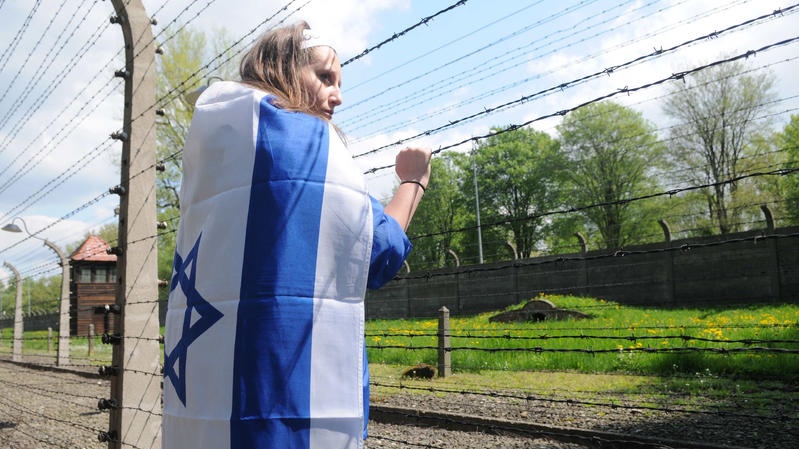 A young Israeli woman wearing the Israeli flag stands next to a barbed wire outside a Nazi death camp in Poland. Photo by Yossi Zeliger/FLASH90