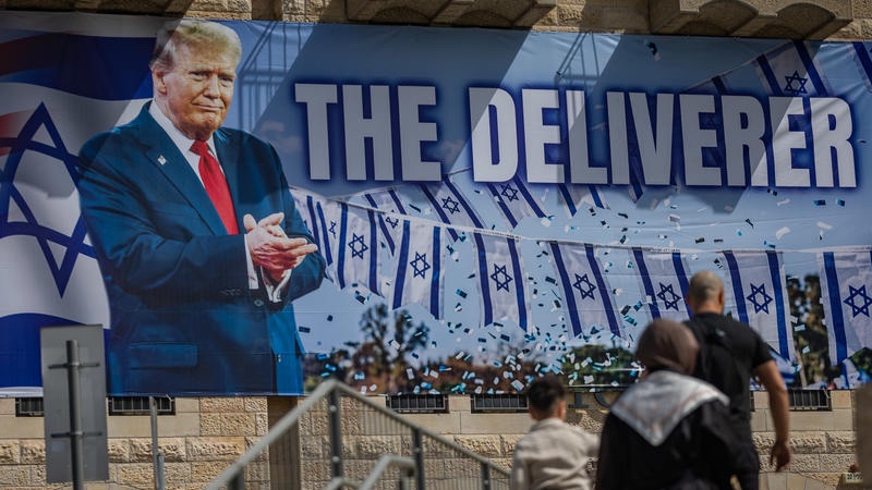 Pepole walk next to a large banner depicting U.S. President Donald Trump with the slogan “The Deliverer” hangs on a building in Jerusalem, April 19, 2026. Photo by Yonatan Sindel/Flash90