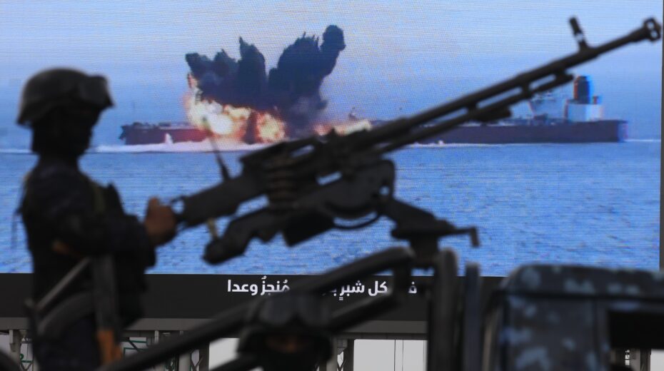 A Houthi fighter stands by a machine gun in front of a digital propaganda screen showing a burning ship in the Red Sea – photographed at a solidarity rally with Hezbollah in Sana'a, Yemen, on April 17, 2026. Photo: EPA/YAHYA ARHAB