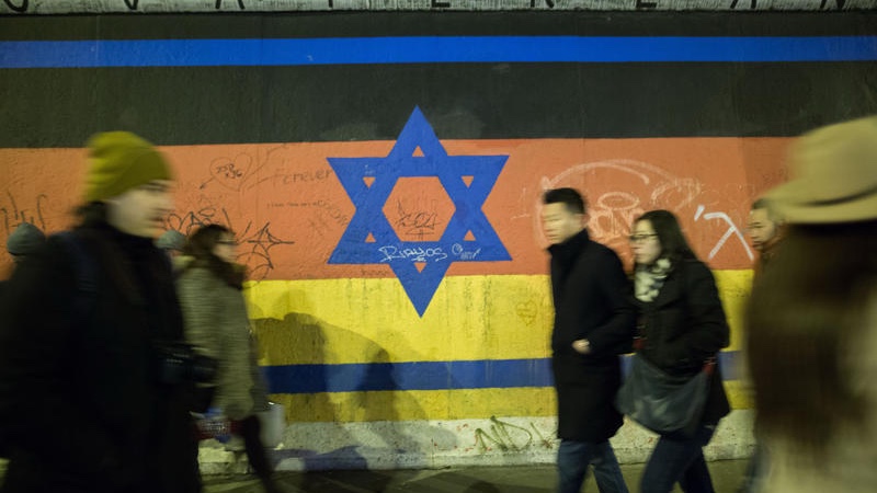 People walk by a mural depicting a combination of the Israeli and German flag on the Berlin Wall. March 13, 2016. Photo by Noam Revkin Fenton/FLASH90