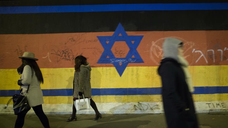 People walk by a mural depicting a combination of the Israeli and German flag on the Berlin Wall. March 13, 2016. Photo by Noam Revkin Fenton/FLASH90
